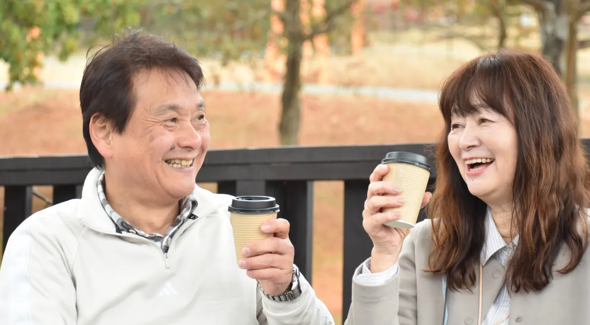 写真：飲み物を持ってにこやかに談笑している、年齢が高めの男女